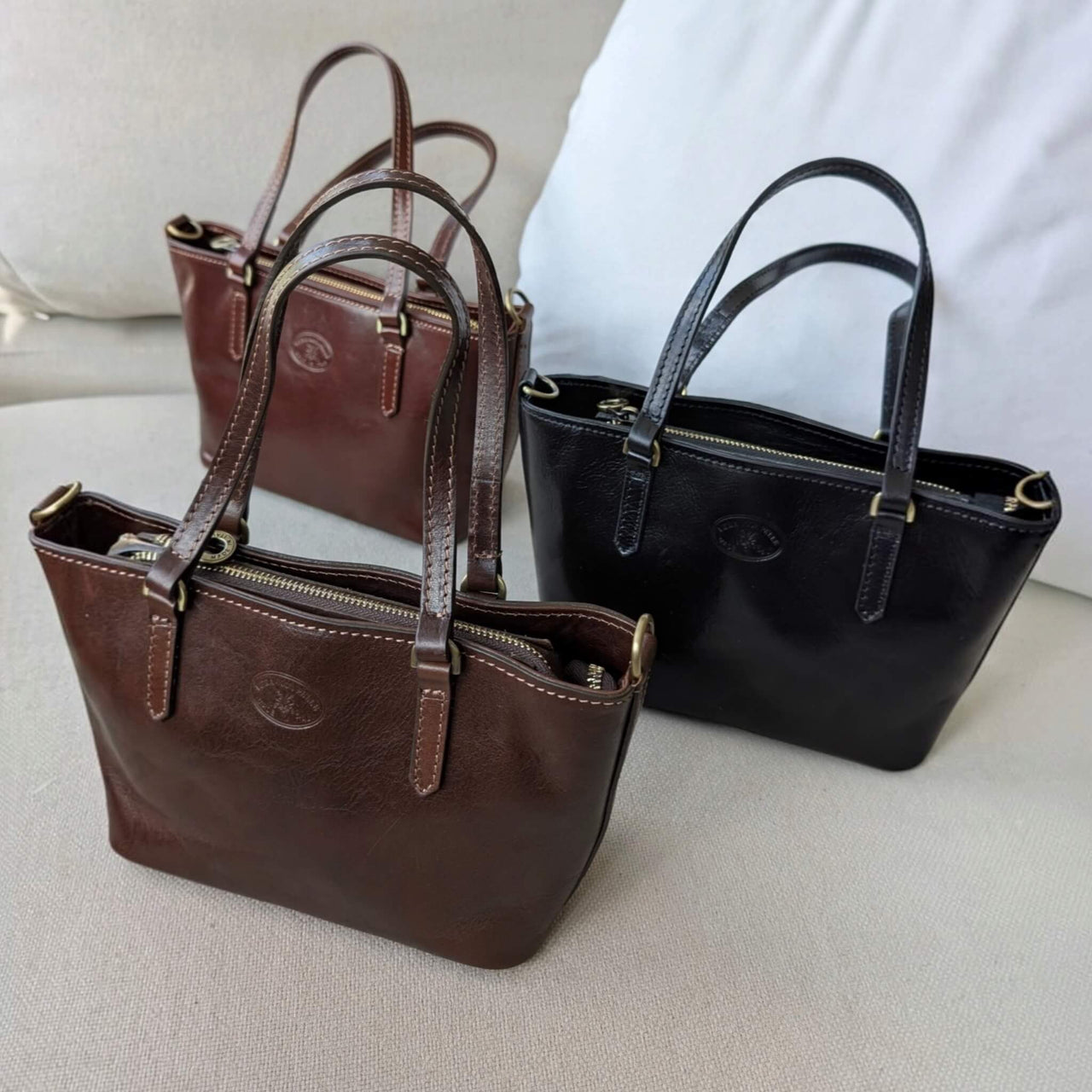 Isual Handtaschen in Schwarz, Schokobraun und Dunkelbraun auf einem Sofa, House of Enira