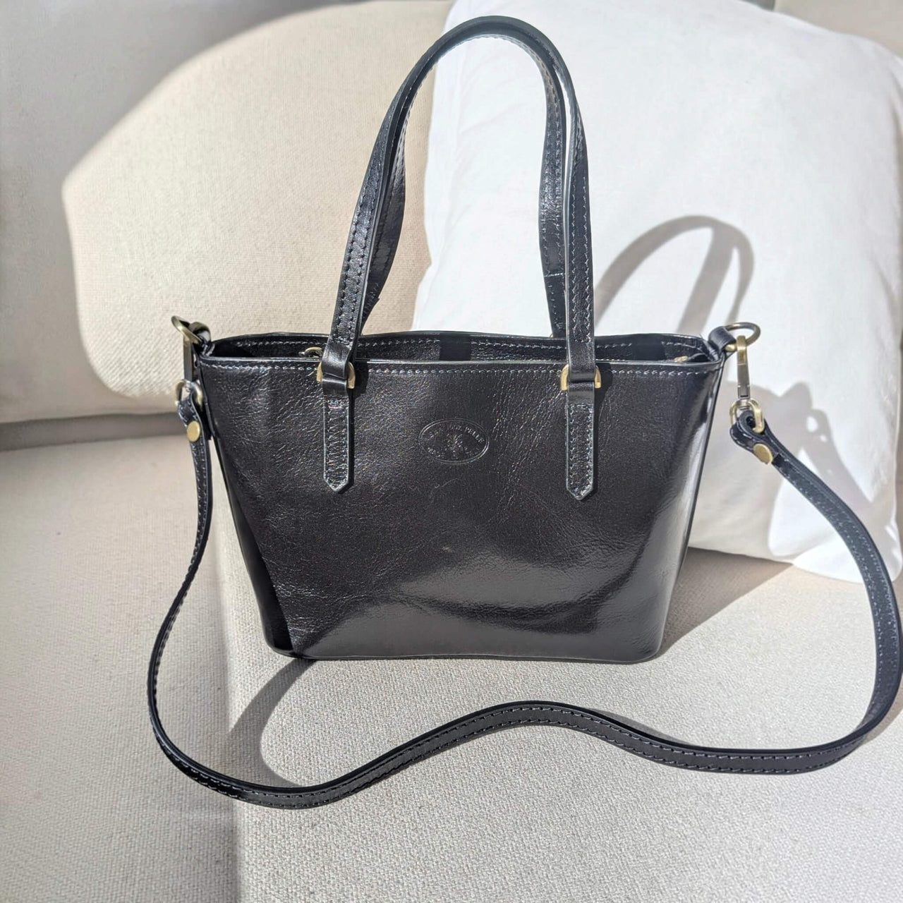 Black leather handbag, in sunlight with the shoulder strap attached, House of Enira Isual