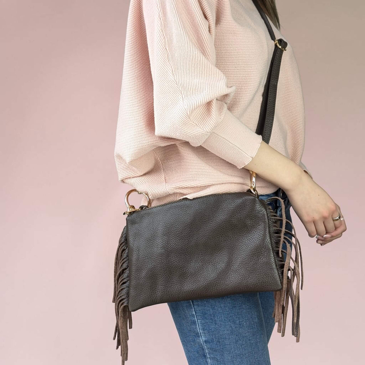 Person wearing a dark brown handbag with fringe details on a pink background