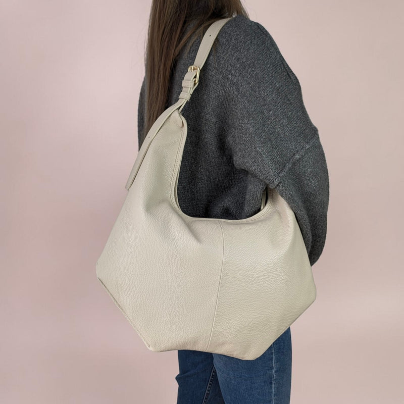 Person wearing a leather Ivory coloured shoulder bag with adjustable belt system als strap against a plain background
