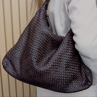 Person wearing chocolate brown leather hobo with weave structure with a neutral background
