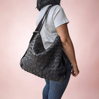 Schultertasche aus geflochtenem Leder in Schwarz, vom Model über der Schulter getragen