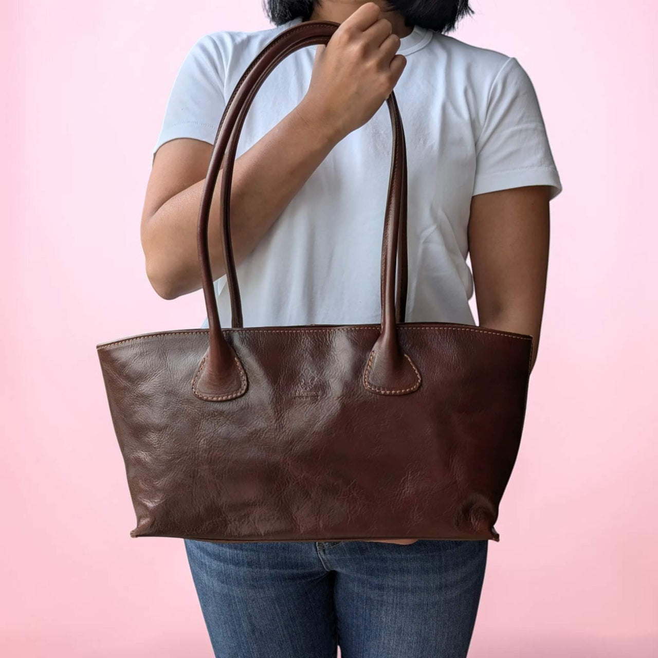 Schultertasche aus Leder in dunklem Kastanienbraun, vom Model in der Hand gehalten