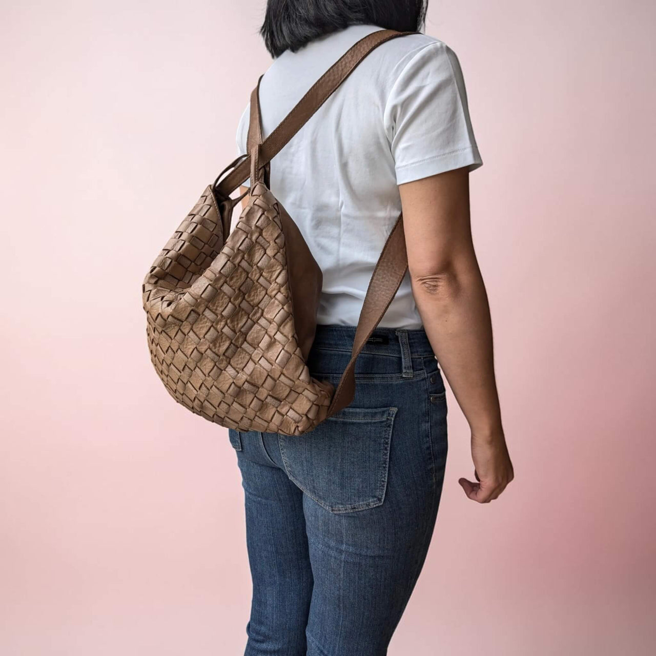 Side view of dark taupe woven leather shoulder bag, worn as a backpack