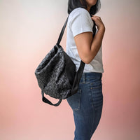 Seitenansicht: Schultertasche aus geflochtenem Leder in Schwarz, auf einer Schulter getragen